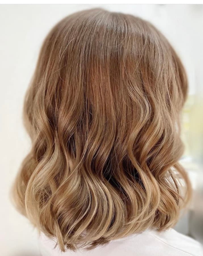 Back view of a woman with wavy brown hair and highlights, styled at a hair salon in Düsseldorf
